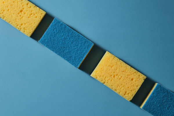A flatlay of blue and yellow dish washing sponges are put in a row on a blue surface